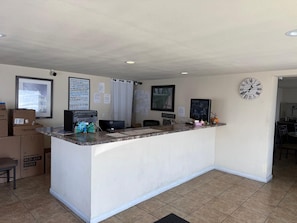 Un espace d’accueil avec un comptoir, une horloge et un tableau encadré au mur.