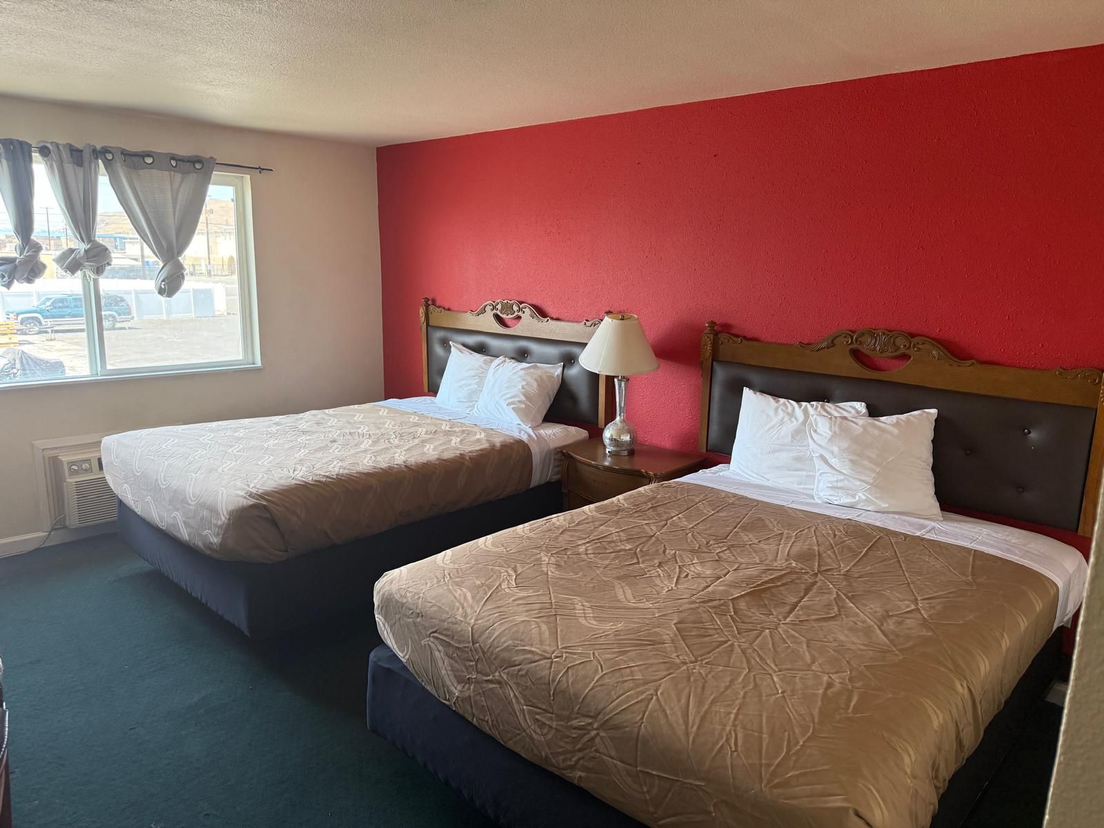 A hotel room with two beds, a red wall, and a window with curtains.