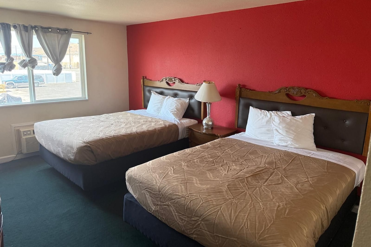 Une chambre d’hôtel avec deux lits, un mur rouge et une fenêtre avec des rideaux.
