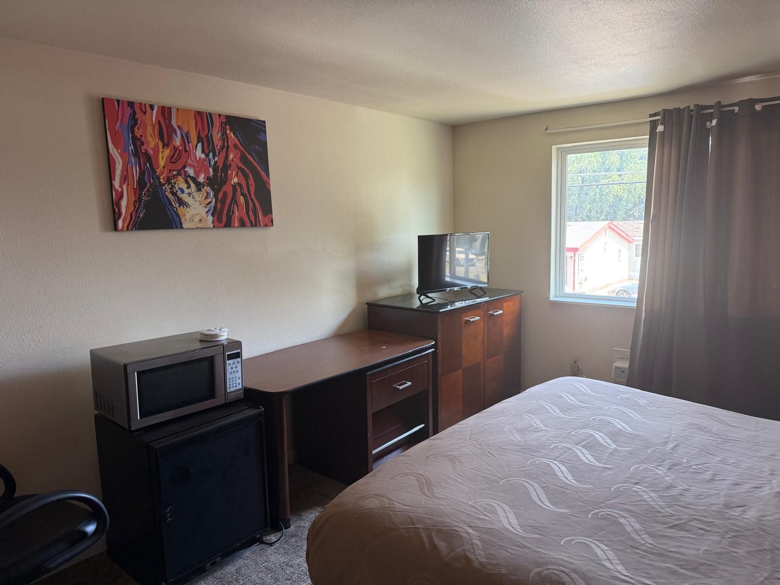 A hotel room with a bed, a desk with a microwave, a television, and a painting on the wall.