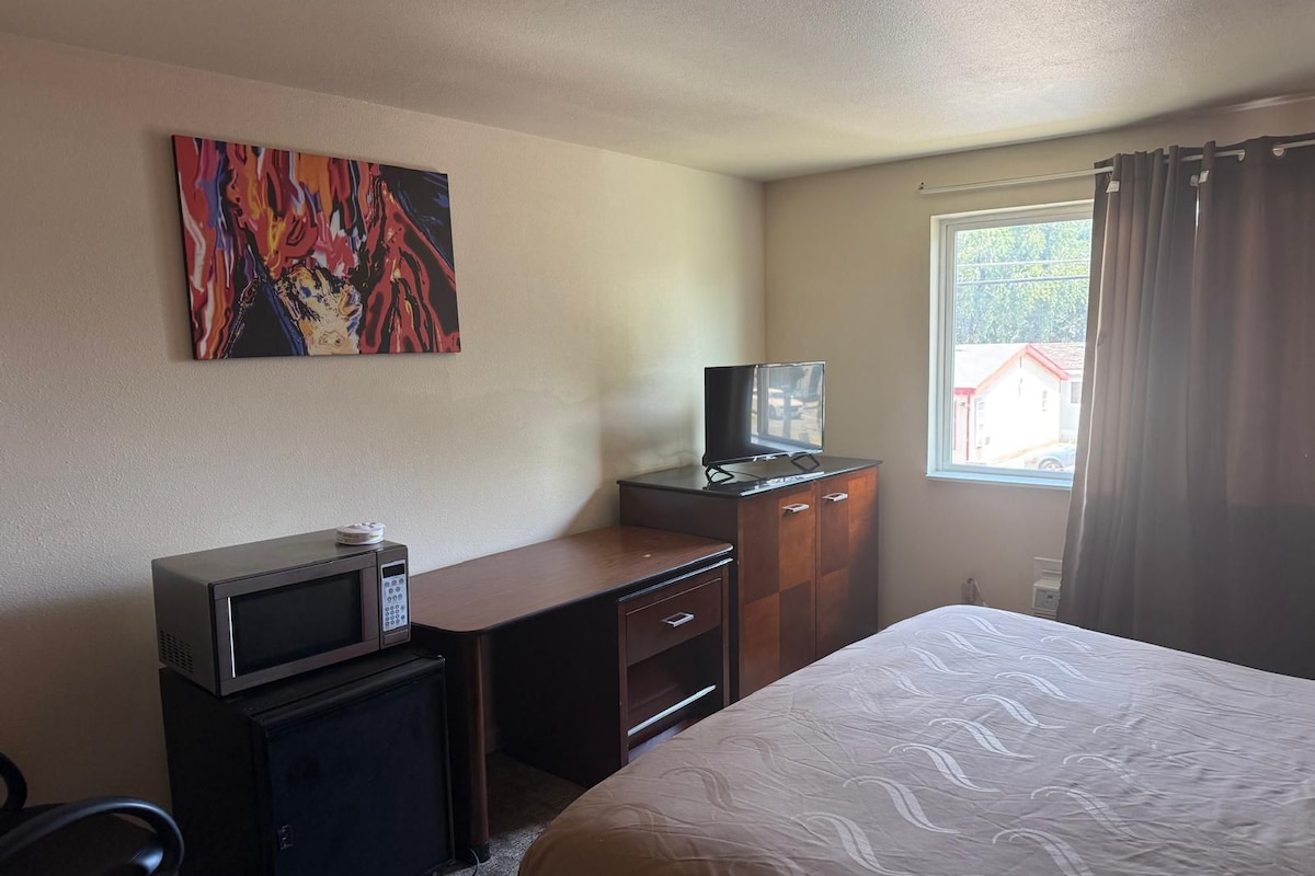 Une chambre d’hôtel avec un lit, un bureau doté d’un micro-ondes, une télévision et un tableau accroché au mur.
