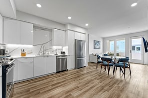 A modern kitchen with white cabinetry, stainless steel appliances, and a dining area with blue chairs and a wooden table.