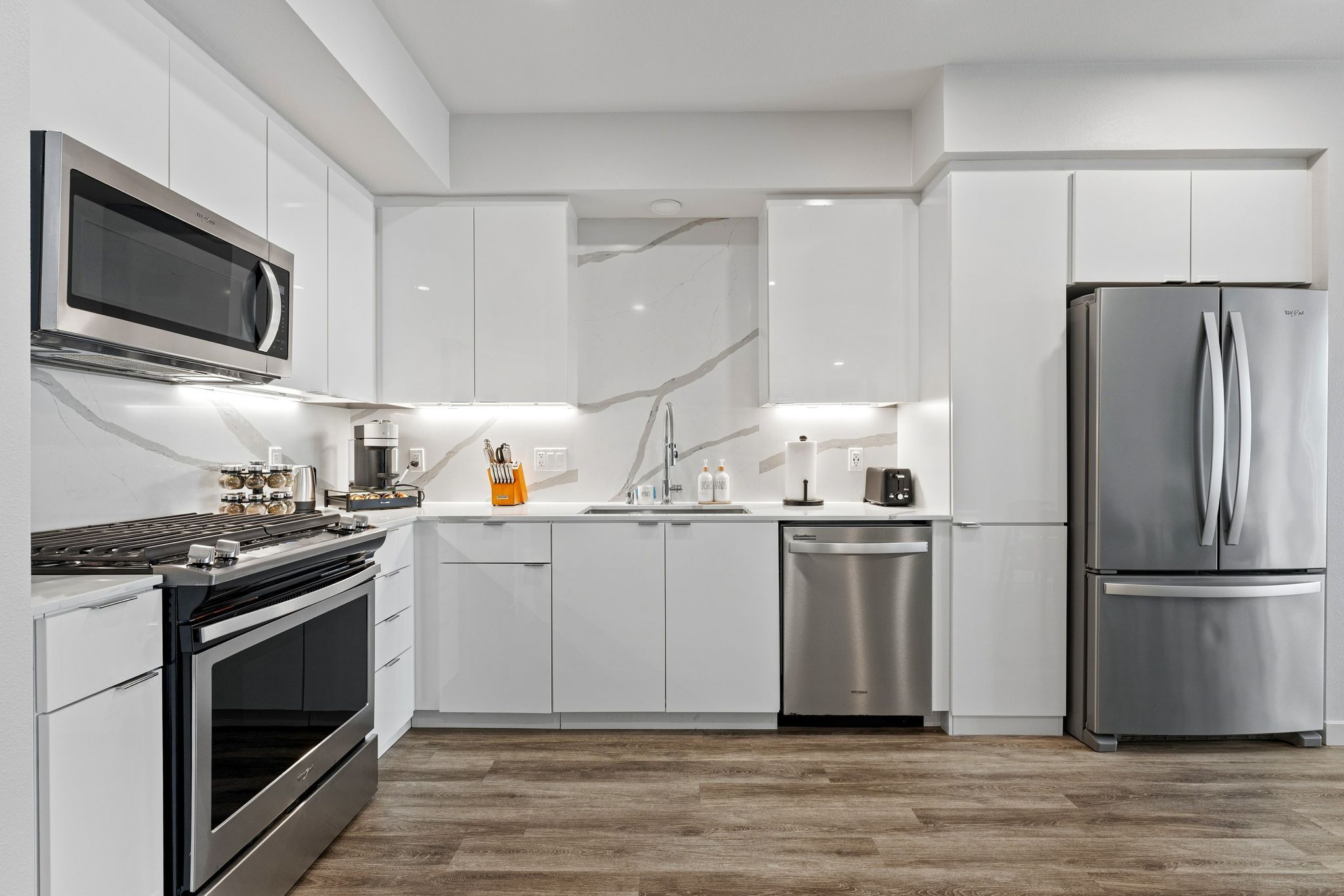 A modern kitchen with white cabinetry, stainless steel appliances, and a wooden floor.