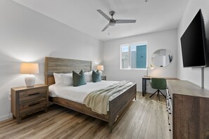 A bedroom with a wooden bed, nightstands, a desk, a chair, a ceiling fan, a TV, and a window with blinds.