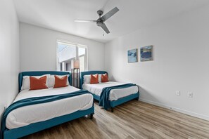 A bedroom with two beds, a ceiling fan, a window, and two wall-mounted artworks.