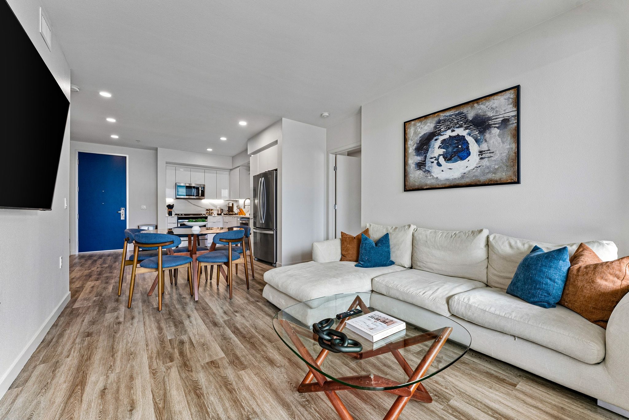 A modern living room with a white sofa, glass coffee table, and a blue door in the background.