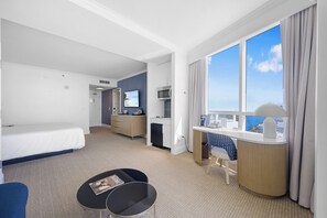 A hotel room with a bed, a desk, a chair, a TV, and a large window with a view. - Oceanview Studio at Fontainebleau Miami Beach with Balcony (Miami Beach)