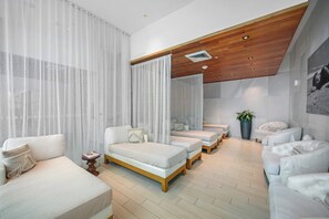 A modern hotel room with a large bed, two smaller beds, a sofa, a chair, a small table, and a large potted plant. - Oceanview Studio at Fontainebleau Miami Beach with Balcony (Miami Beach)