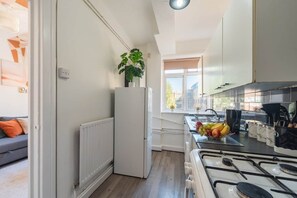 Eine kleine Küche mit einem weißen Kühlschrank, einem Gasherd und einem Fenster für natürliches Licht.
