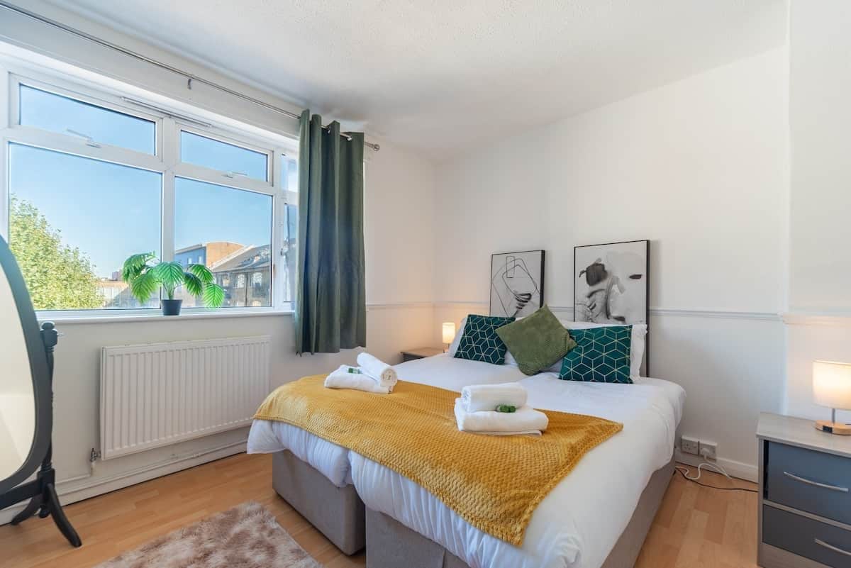 A bedroom with a bed, a window, a radiator, a bedside table, and a lamp.