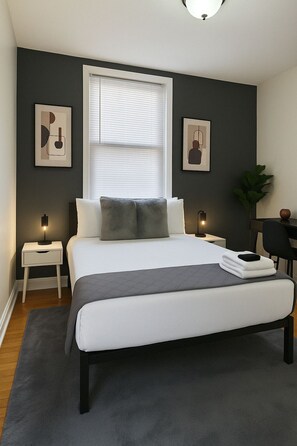 Een moderne slaapkamer met een groot bed, nachtkastjes, een raam met zonwering en twee kunstwerken aan de muur.