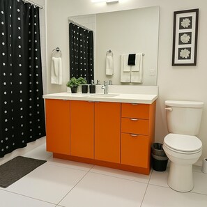 A bathroom with a white toilet, an orange cabinet, a black and white polka dot shower curtain, and a framed floral decoration on the wall. - Elegant 2BR Apartment w/ In-Unit Laundry (Chicago)