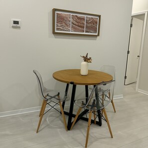Een eethoek met een ronde tafel, vier stoelen, een vaas met een plant en een lijst met een foto aan de muur.