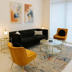 A modern living room with a black sofa, a yellow armchair, a glass coffee table, and abstract paintings on the wall. - Elegant 2BR Apartment w/ In-Unit Laundry (Chicago)