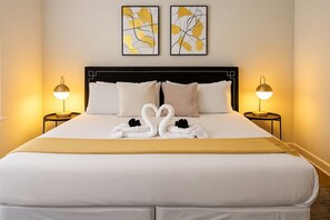 A hotel room with a large bed, two bedside lamps, and two abstract paintings on the wall. - Cozy 2BR Apt for a Seamless Stay (Chicago)