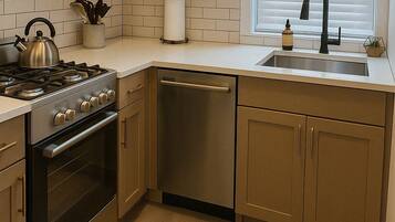 A modern kitchen with stainless steel appliances, wooden cabinets, and a window with blinds.