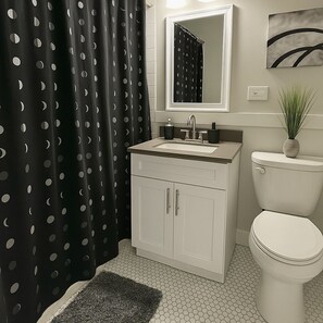 Een badkamer met een witte wastafel, toilet, douchegordijn met zwart-wit stippen, spiegel en een plant op het toilet.