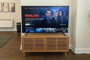 Een televisie op een houten standaard die een film toont genaamd 'MOBLAND', met een synopsis en opties om af te spelen of verder te kijken.