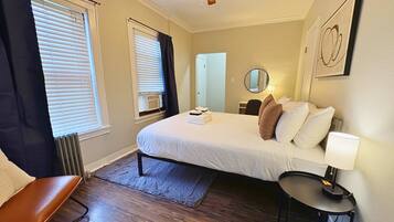 Ein Hotelzimmer mit einem Bett, einem Schreibtisch, einem Sessel, einer Stehlampe und einem Deckenventilator.