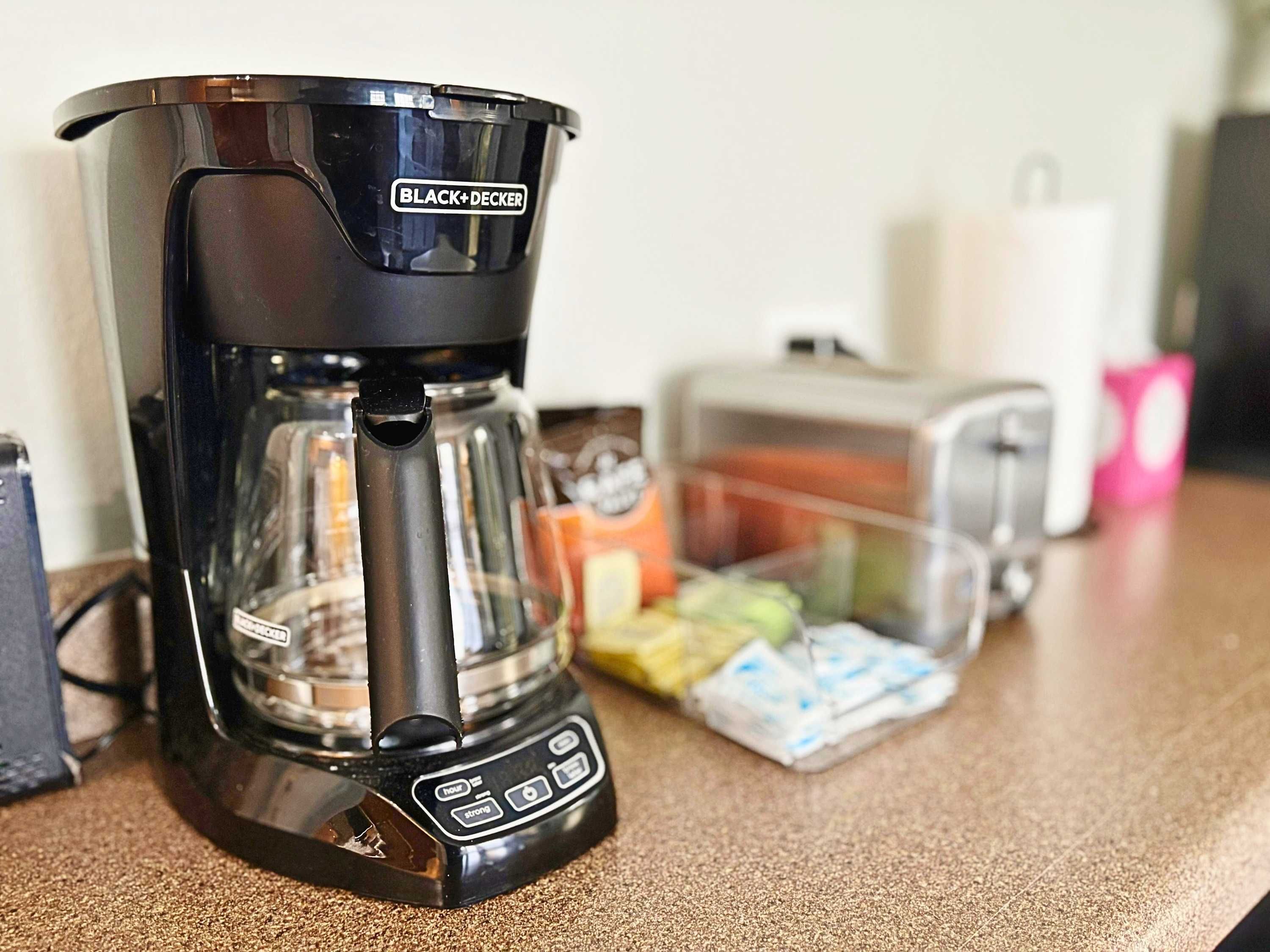 A BLACK+DECKER coffee maker on a kitchen counter with a toaster and food items in the background.