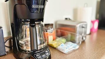 A BLACK+DECKER coffee maker on a kitchen counter with a toaster and food items in the background.