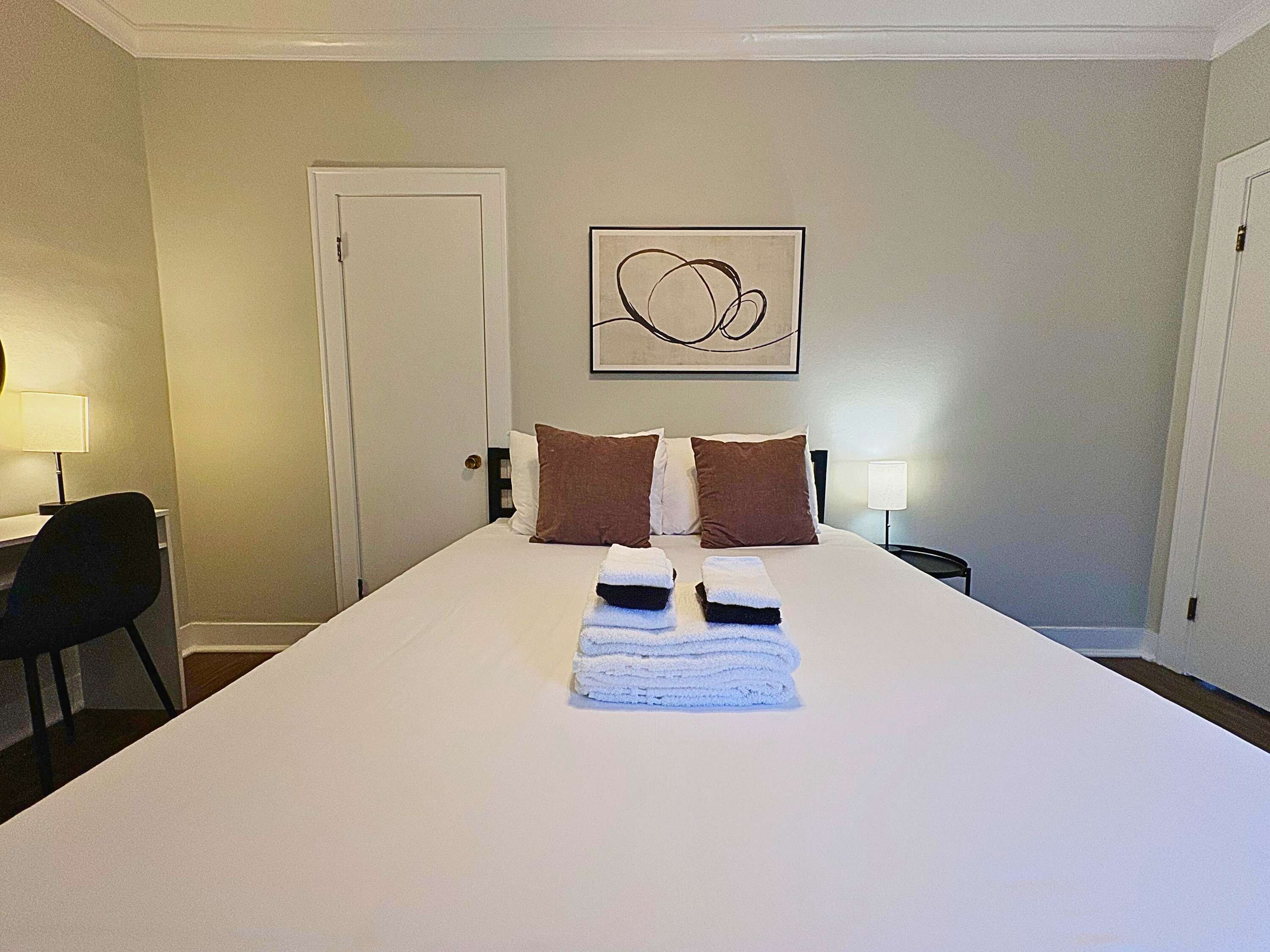 A hotel room with a large bed, two pillows, a bedside table with a lamp, and a door.