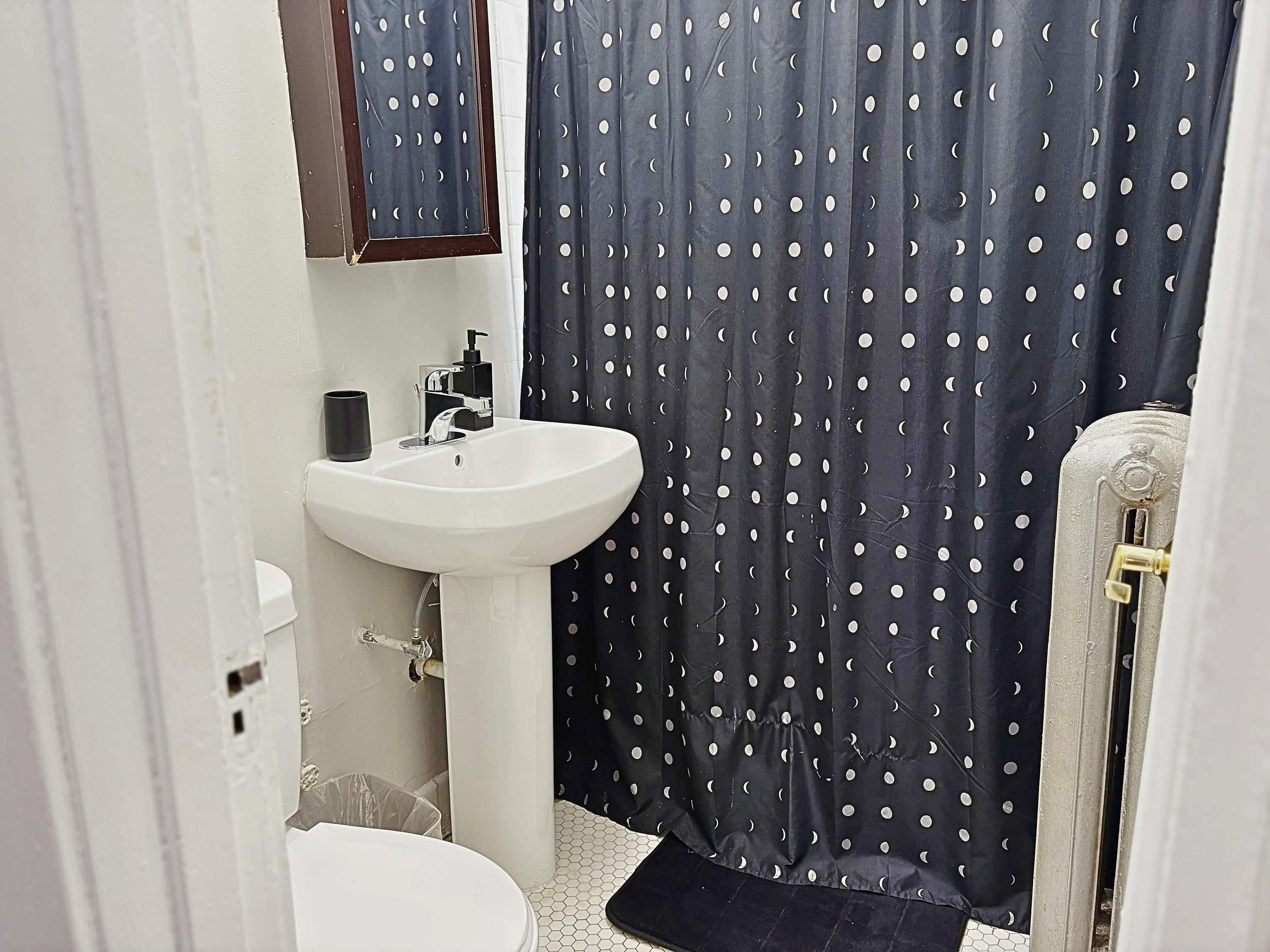 A bathroom with a white sink, a mirror above it, and a dark curtain with a moon pattern.