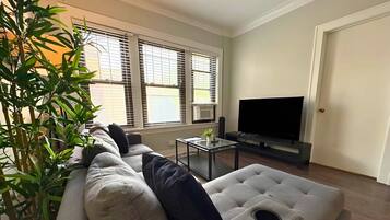Uma sala de estar com sofá seccional, televisão de tela plana, mesa de centro e planta em vaso.