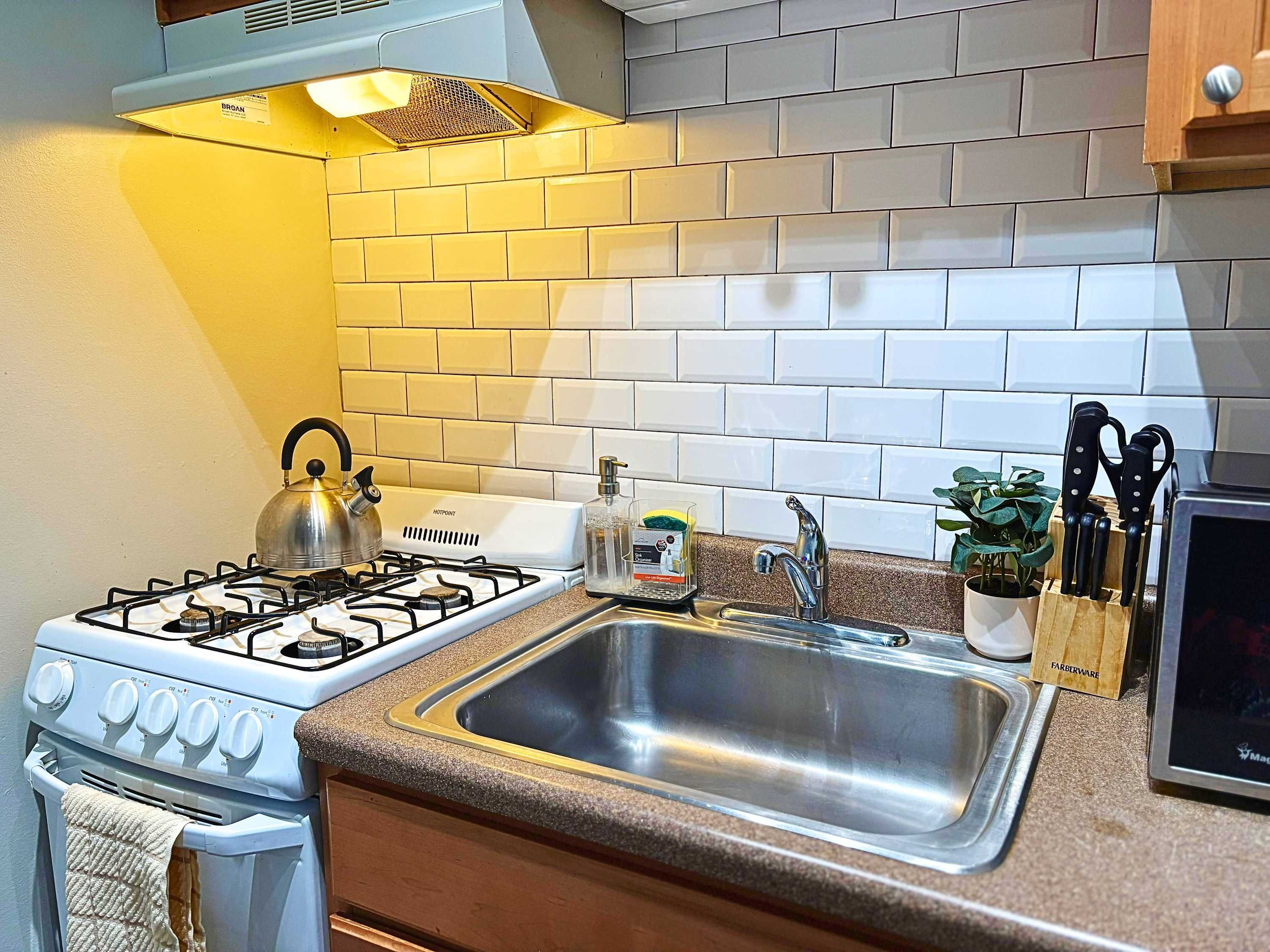 A kitchen with a gas stove, a stainless steel sink, and a brick backsplash.