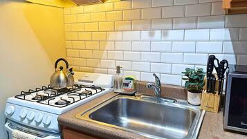 A kitchen with a gas stove, a stainless steel sink, and a brick backsplash.