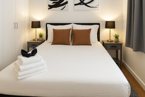 Une chambre d’hôtel avec un lit, deux tables de chevet, des lampes, une plante et des œuvres d’art accrochées au mur.