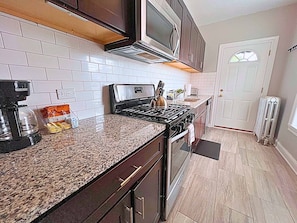 A kitchen with a granite countertop, stainless steel appliances, and white subway tiles. - Modern City Vibes | 1BR Stay (Chicago)
