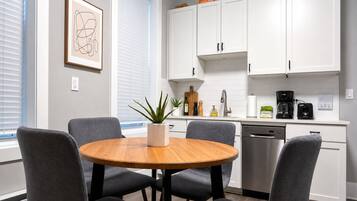 Una cocina moderna con armarios blancos, una mesa redonda de madera y sillas grises.