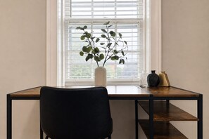 A room with a desk, chair, window with blinds, and a plant.