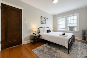 A bedroom with a bed, bedside tables, a nightstand, a window, and a radiator.