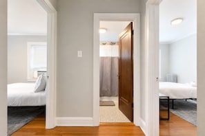 Un corridoio che porta a due camere da letto, ciascuna con un letto, una finestra e un termosifone.