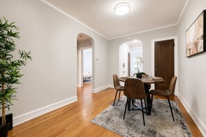 A dining area with a round table, four chairs, a potted plant, and a rug.