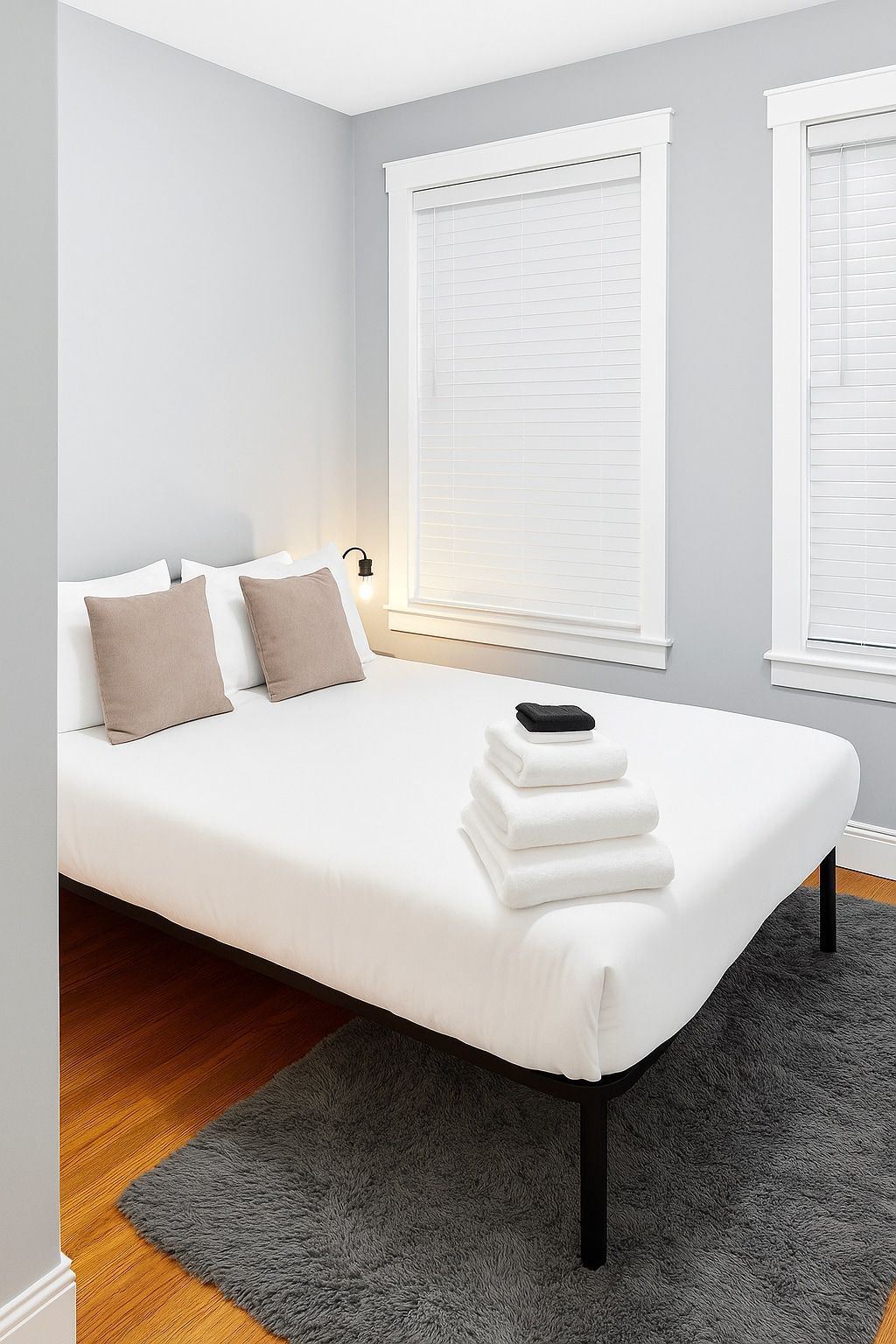 Ein modernes Schlafzimmer mit einem Bett, zwei Kissen, einer Nachttischlampe und einem Stapel Handtücher.