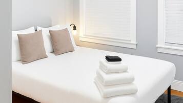 Ein modernes Schlafzimmer mit einem Bett, zwei Kissen, einer Nachttischlampe und einem Stapel Handtücher.