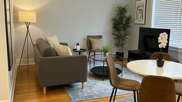 Ein stilvolles Wohnzimmer mit einer Couch, Sesseln, einem Couchtisch, einem Fernseher und einer Pflanze.