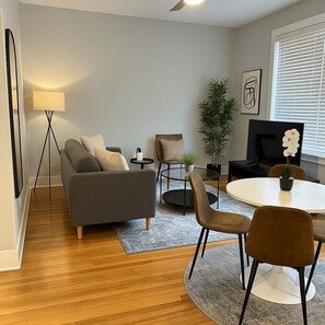 Ein stilvolles Wohnzimmer mit einer Couch, Sesseln, einem Couchtisch, einem Fernseher und einer Pflanze.