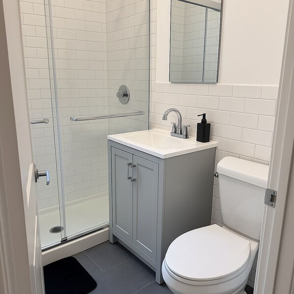 A bathroom with a glass shower enclosure, a white sink with a soap dispenser, and a toilet.