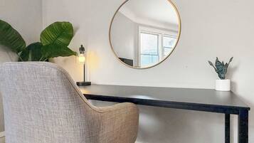 A room with a round mirror, a desk, a chair, a potted plant, and a small table with a plant.