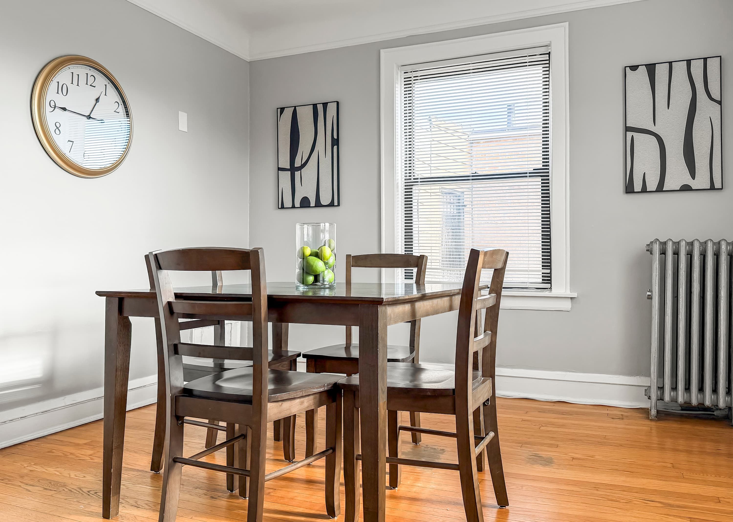 A dining room with a wooden table and chairs, a clock on the wall, and abstract art pieces.
