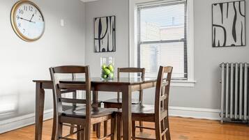 A dining room with a wooden table and chairs, a clock on the wall, and abstract art pieces.