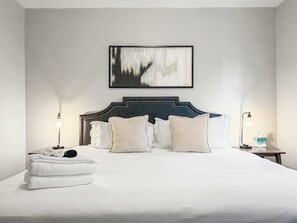 Un lit bien fait, avec du linge de lit blanc, une tête de lit sombre et deux lampes de chevet.