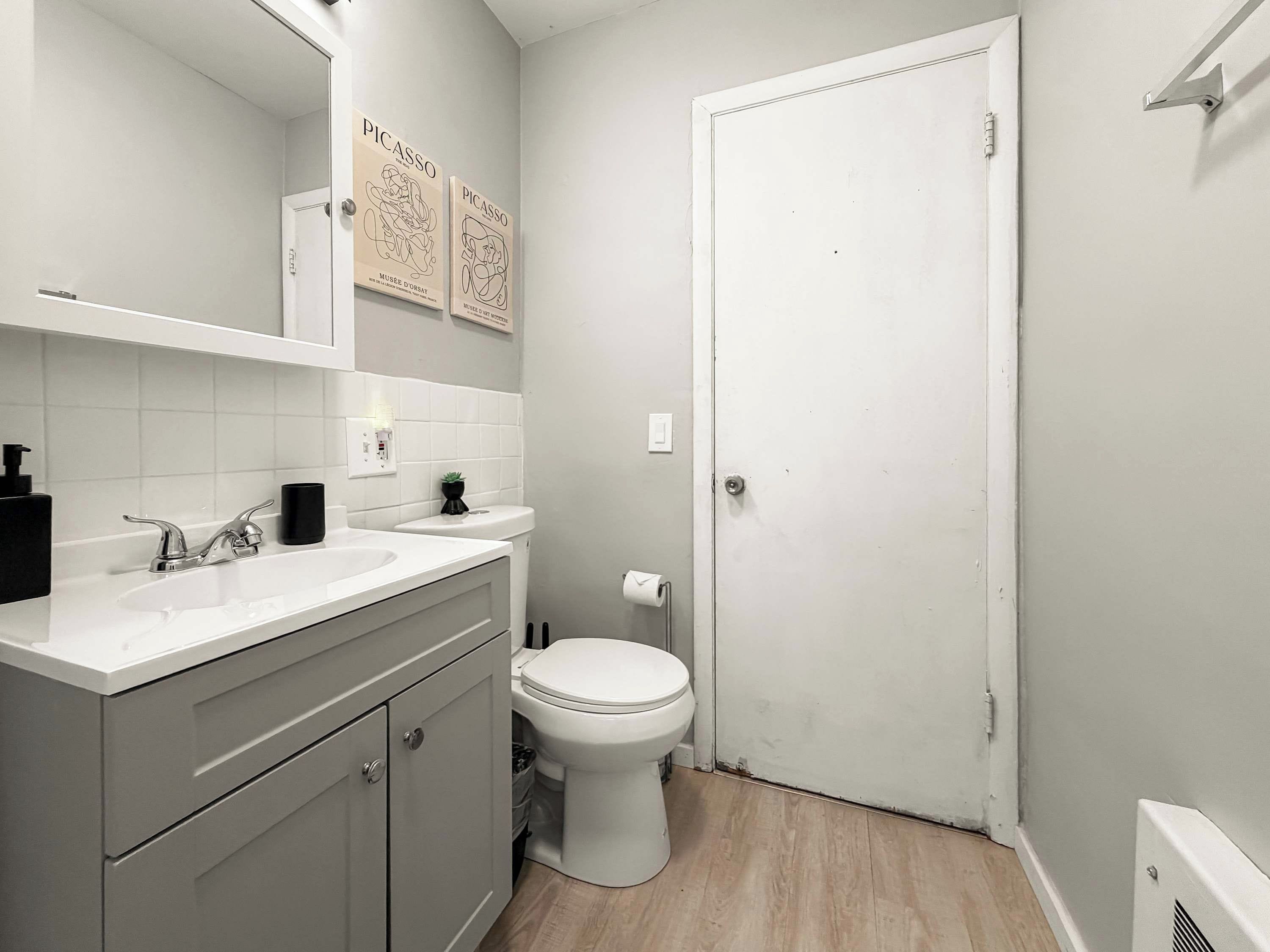 A modern bathroom with a white sink, mirror, and toilet. There are two framed artworks on the wall above the mirror.