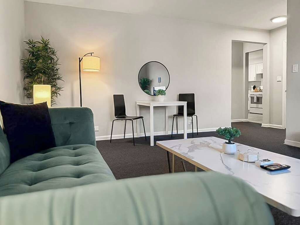 A modern living room with a green sofa, a white coffee table, and a dining area with two chairs and a small table.