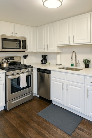 A modern kitchen with white cabinetry, stainless steel appliances, and a wooden floor. - 2BR Calm & Aesthetic Apt (Chicago)