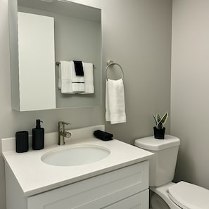 Un bany modern amb un lavabo blanc, un mirall, un vàter i una planta en test.